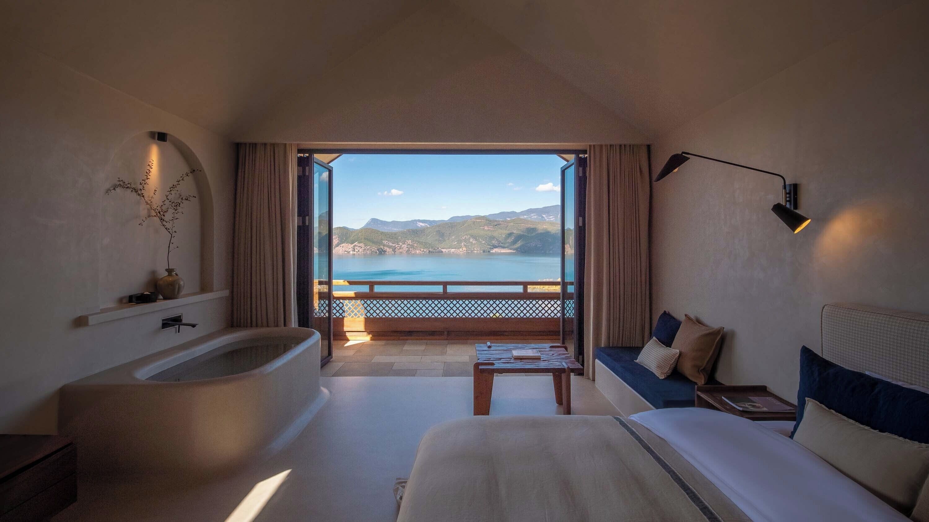 Quarto de hotel com uma banheira grande, um sofá, uma mesa pequena e vista para o mar.