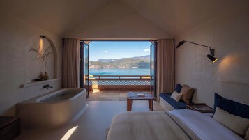 Quarto de hotel com uma banheira grande, um sofá, uma mesa pequena e vista para o mar.