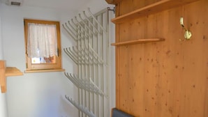 Une pièce avec un mur en bois, une fenêtre ornée d’un rideau en dentelle, un radiateur blanc et un canapé gris.