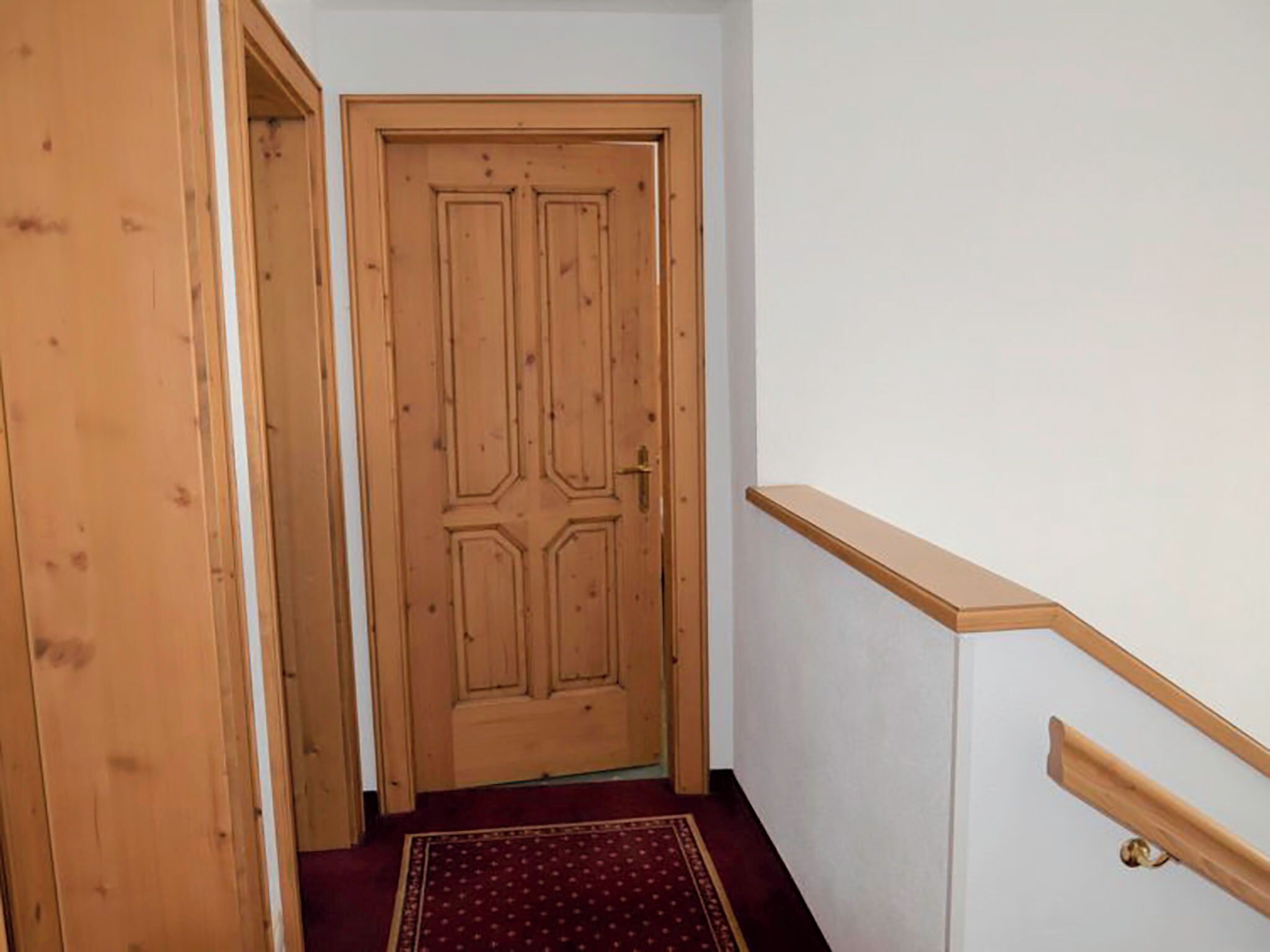 Eine Holztür mit schlichtem Design, ein Teppichboden und ein Holzhandlauf auf der rechten Seite.