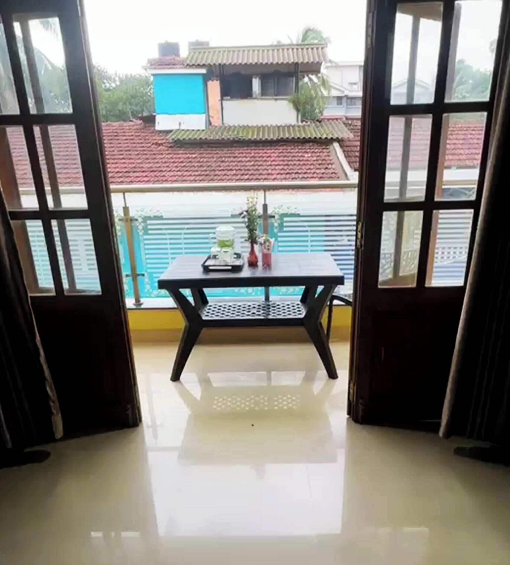 A room with a table and chairs, a view of buildings outside, and a balcony with a railing.