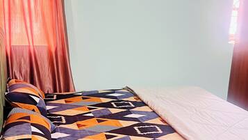 A room with a bed, a patterned blanket, a curtain, and an air conditioning unit.