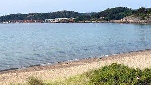 A beach with a calm sea, sandy shore, and buildings in the background. - Cozy home in Lindesnes with WiFi (Lindesnes)