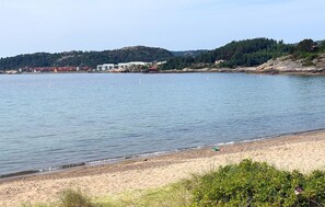Una playa con mar tranquilo, orilla de arena y edificios al fondo.