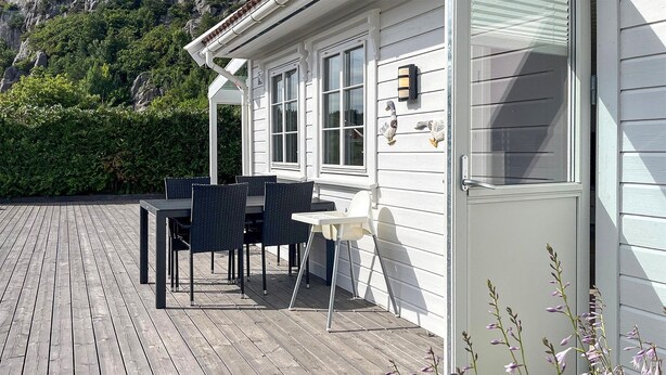 A wooden deck with a table and chairs, a white building with windows, and a door. - Cozy home in Lindesnes with WiFi (Lindesnes)