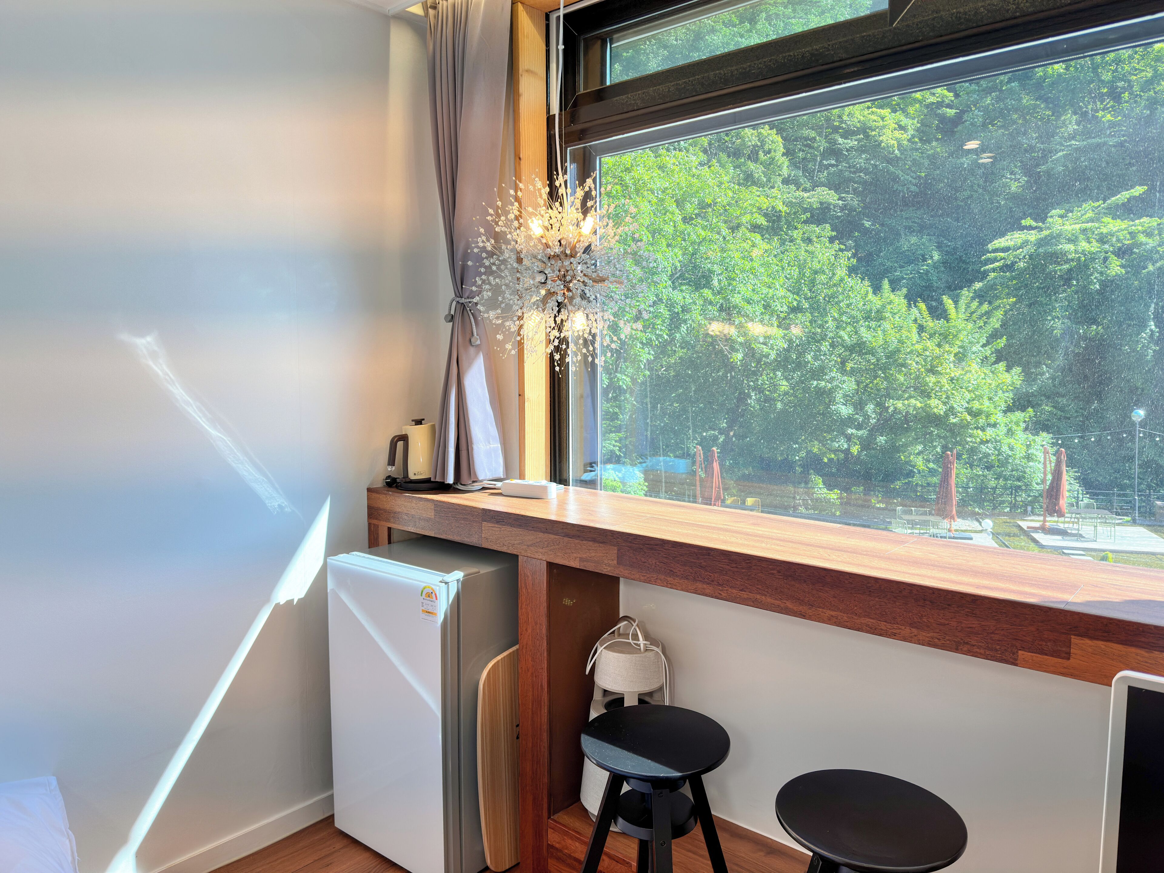 Habitación compacta con un mostrador de madera, un refrigerador pequeño, una silla y una ventana con vistas al verdor.