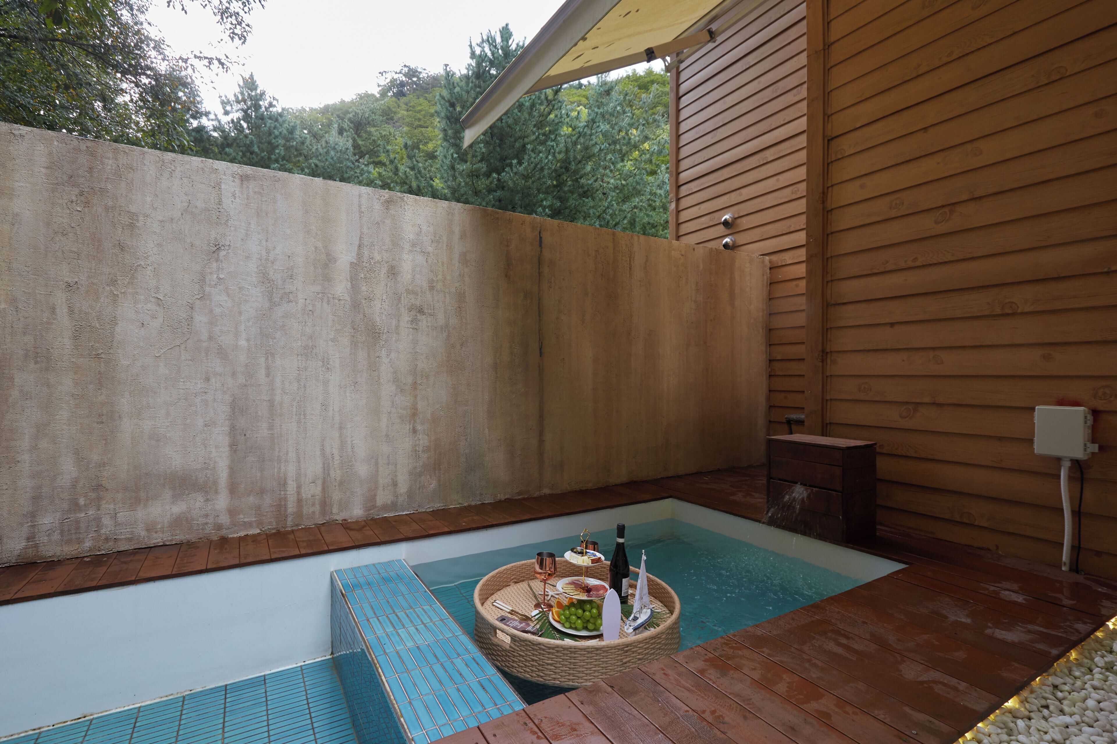 Una piscina con una bandeja flotante de comida y bebidas, una terraza de madera y un muro de concreto.