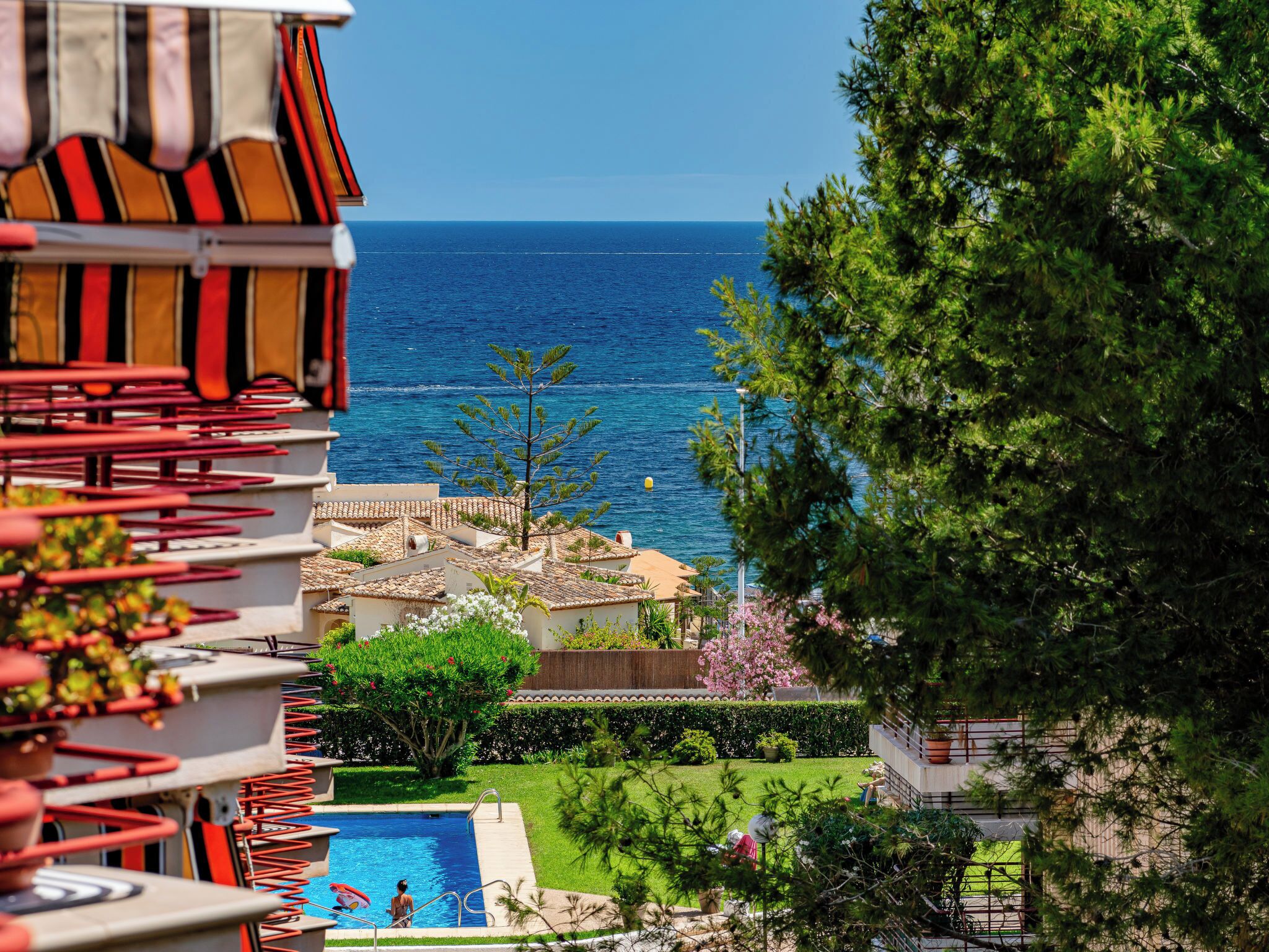 A pool area with a view of the sea, surrounded by greenery and buildings.