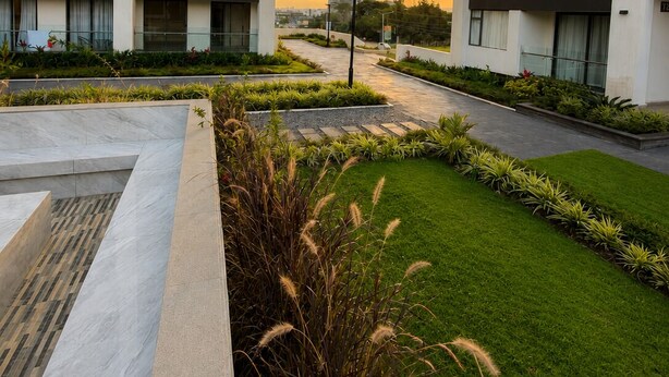 Un moderno edificio de apartamentos con varios balcones, un jardín ajardinado y una vista despejada del atardecer.