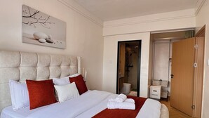Habitación de hotel con una cama grande, un candelabro, un cuadro en la pared y un baño visible a través de una puerta abierta.