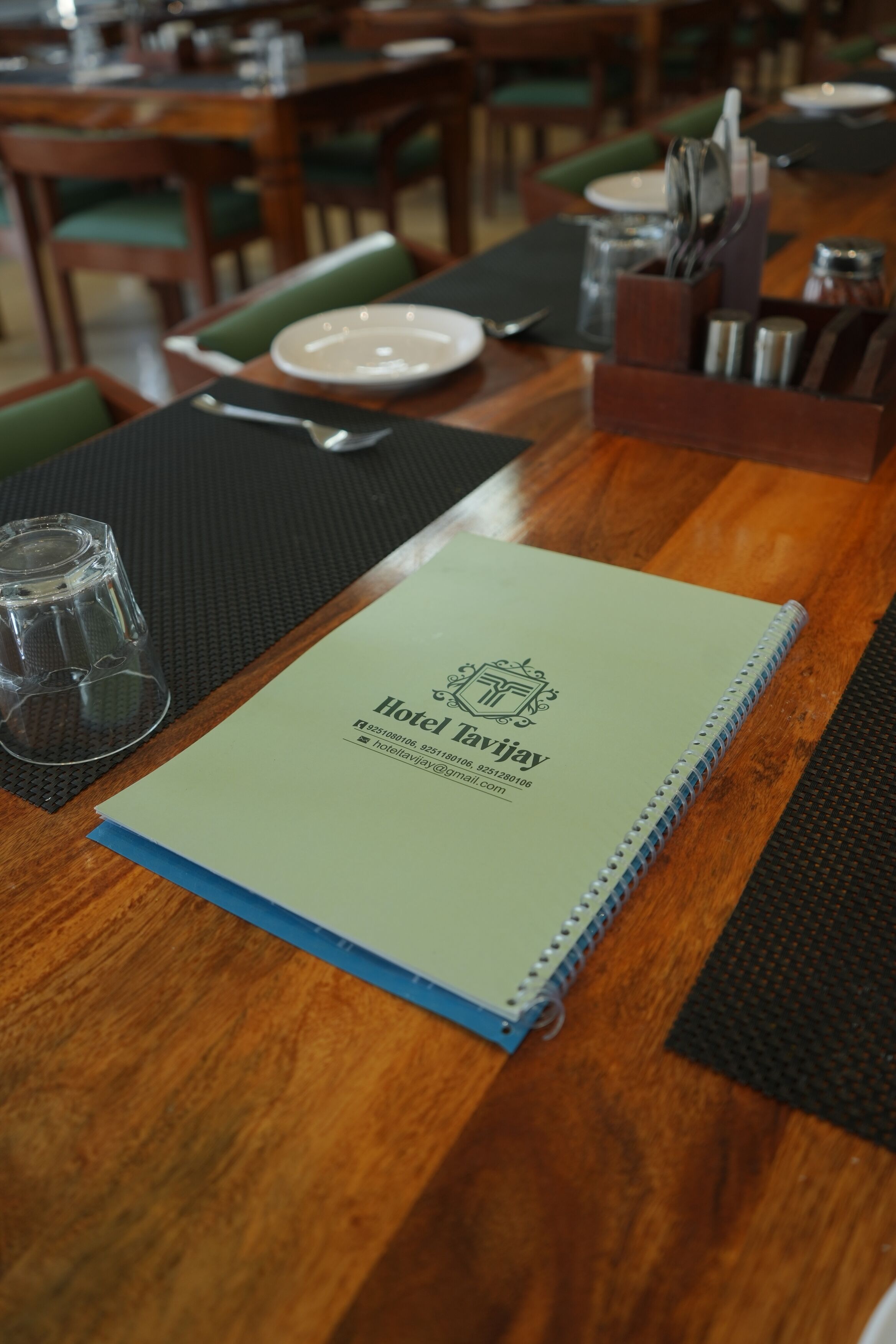 A hotel brochure on a wooden table with a glass, a plate, and cutlery.