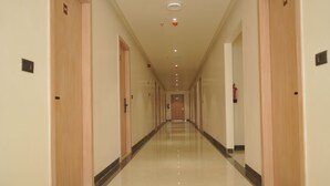 A long, narrow hotel corridor with wooden doors on either side, a shiny tiled floor, and a ceiling with recessed lighting.