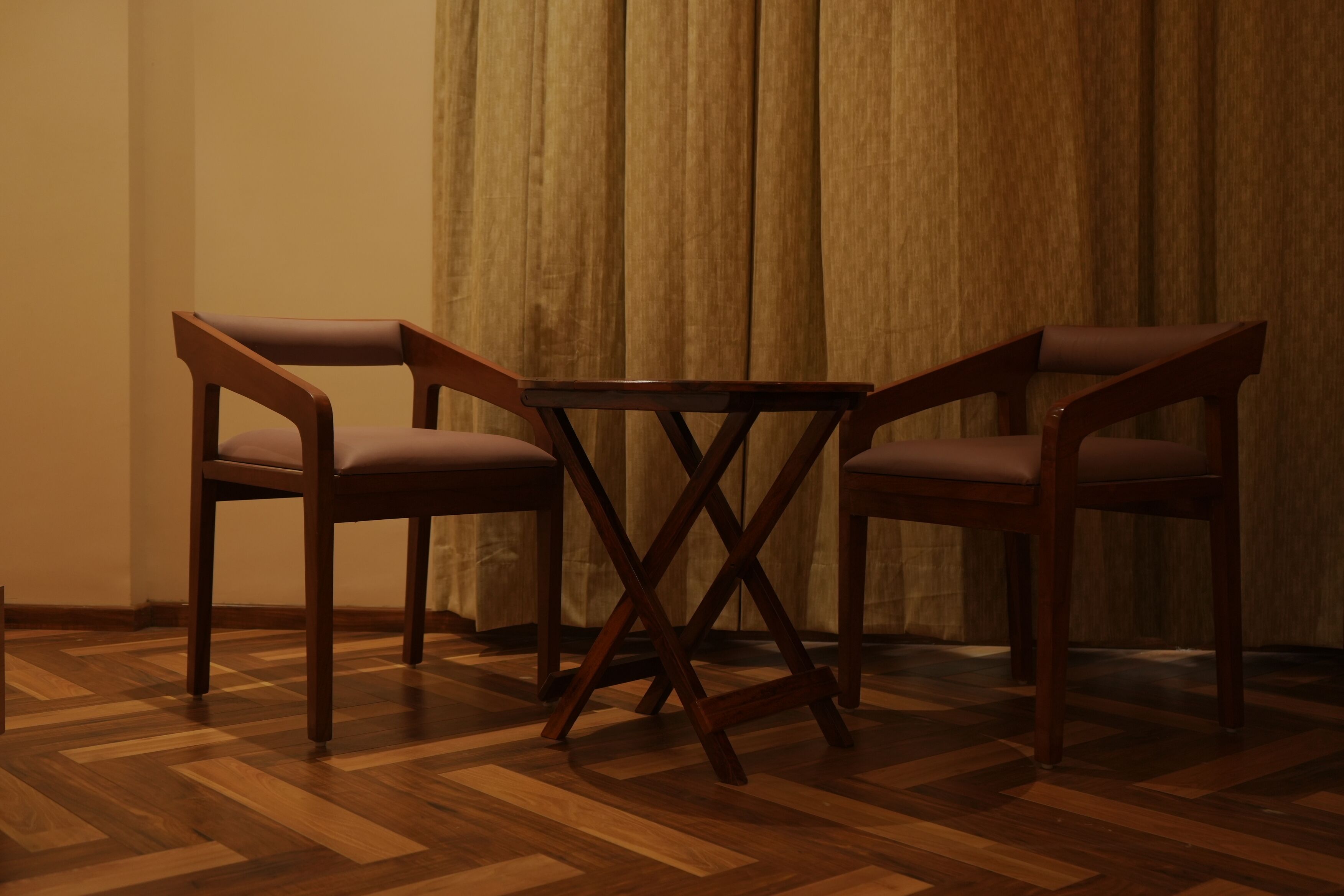 Une pièce dotée d’un parquet en bois à motifs en chevrons, d’une petite table ronde et de trois chaises avec des sièges rembourrés.