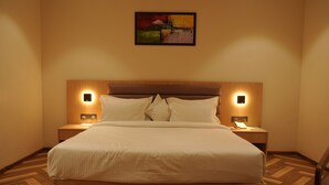 A hotel room with a large bed, two bedside tables, a headboard, and a painting on the wall.