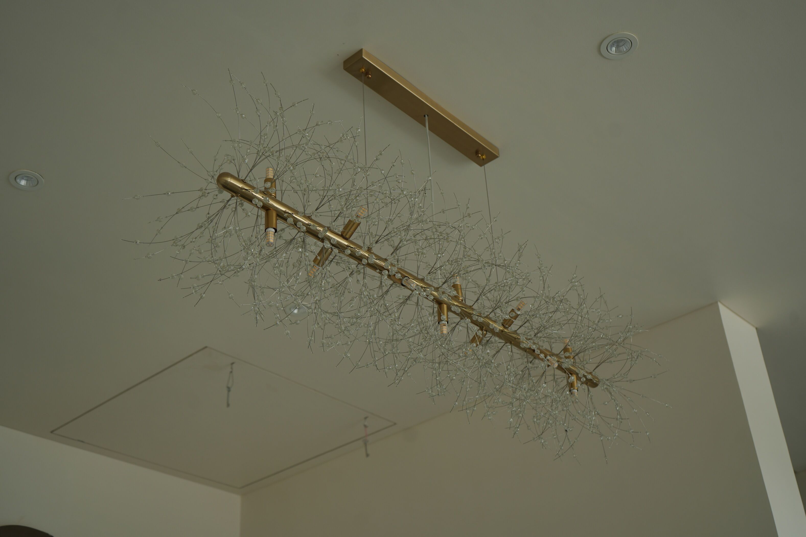 Teto com um lustre com uma haste dourada central e várias ramificações de cristal.