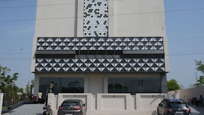 A building with a large vertical panel with a geometric pattern, a flat roof, and a parking area with two cars.