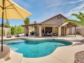 A swimming pool with a curved edge, a covered patio area with outdoor furniture, and a house with a sloped roof. - Private Pool + Spa + Outdoor Kitchen | Near Golf | Endless Summer Oasis (Scottsdale)