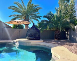 Ein Pool mit Vogelkäfig, Palmen und Sonnenschirm.