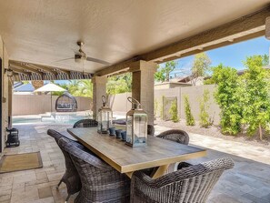 An outdoor patio with a wooden table, wicker chairs, lanterns, and a ceiling fan. - Private Pool + Spa + Outdoor Kitchen | Near Golf | Endless Summer Oasis (Scottsdale)