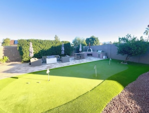 Ein Garten mit Putting-Grün, Gartenmöbeln und einem Hecken.