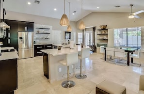 A modern kitchen with stainless steel appliances, a central island with bar stools, pendant lighting, and a dining area with a glass table and chairs. - Private Pool + Spa + Outdoor Kitchen | Near Golf | Endless Summer Oasis (Scottsdale)