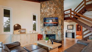 A modern living room with a stone fireplace, leather sofas, a wooden coffee table, and a TV mounted on the wall. - Villa Zephyra, Grand 8BR Villa for Families & Groups (Jensen Beach)