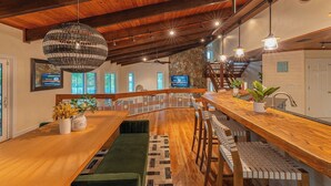 A modern kitchen with a wooden island, pendant lighting, and a stone accent wall. - Villa Zephyra, Grand 8BR Villa for Families & Groups (Jensen Beach)