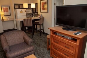 Ein kompaktes Hotelzimmer mit einer Couch, einem Fernseher auf einem Holztischchen, einer kleinen Küchenzeile mit einer Mikrowelle und einem Esstisch mit Stühlen.