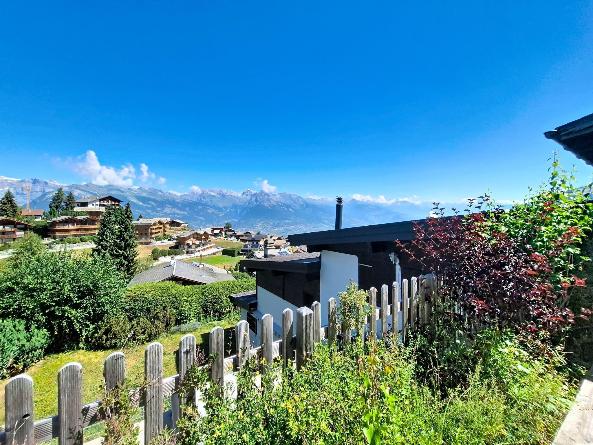 Un paysage montagneux avec une clôture en bois, des bâtiments et un ciel dégagé.