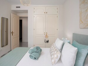 Ein Schlafzimmer mit einem Bett, Kissen, einem zusammengerollten Handtuch, einem Kleiderschrank und einem Spiegel.