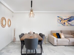 Een eetruimte met een houten tafel, grijze stoelen, een hanglamp en een schilderij aan de muur.