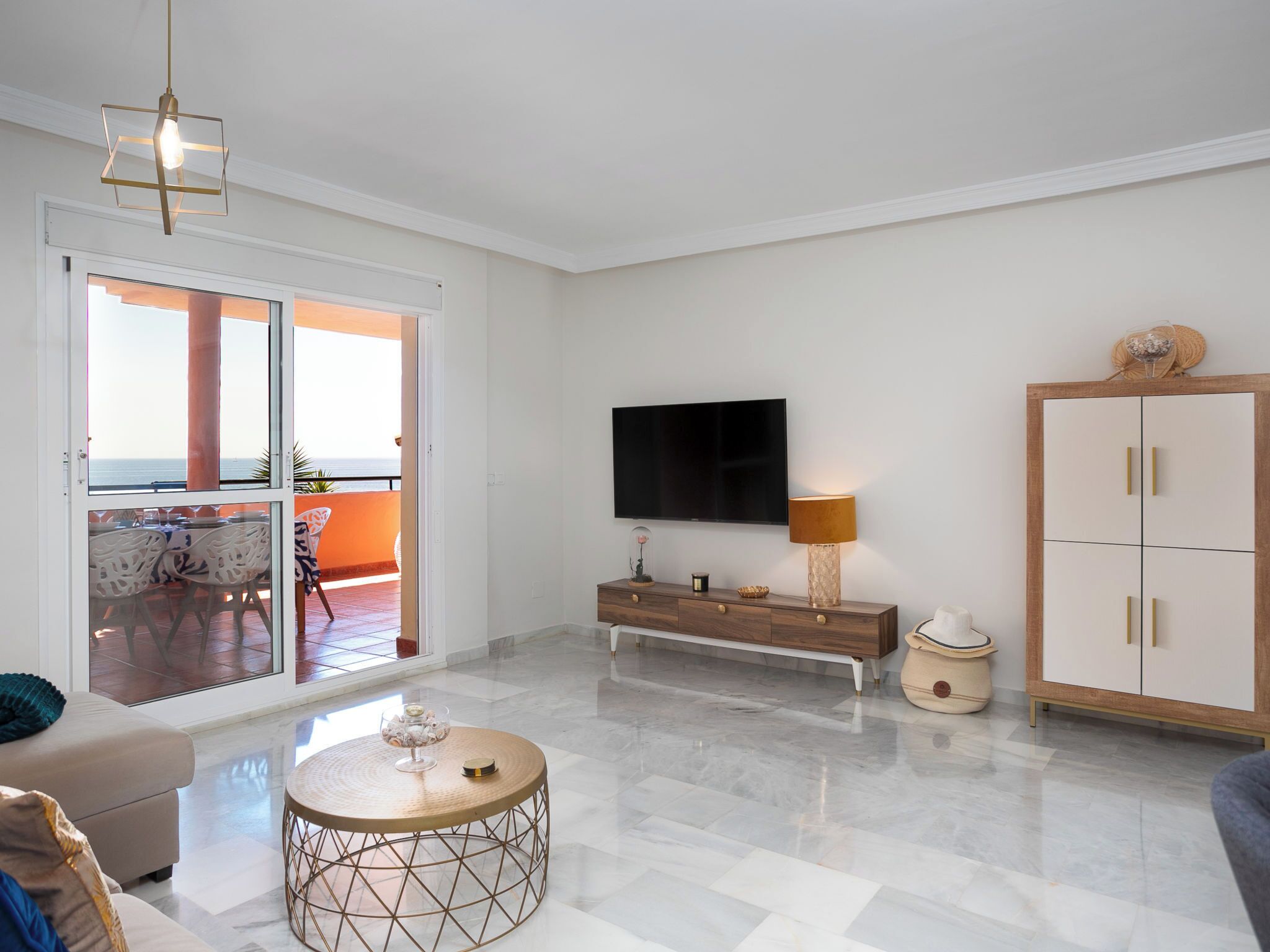 A modern living room with a TV, a wooden cabinet, a round coffee table, and a balcony with a view.