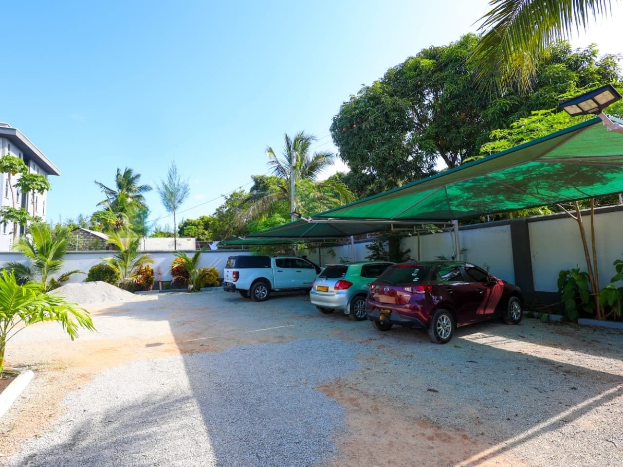 Uma área de estacionamento com três carros, um edifício com telhado verde e palmeiras.