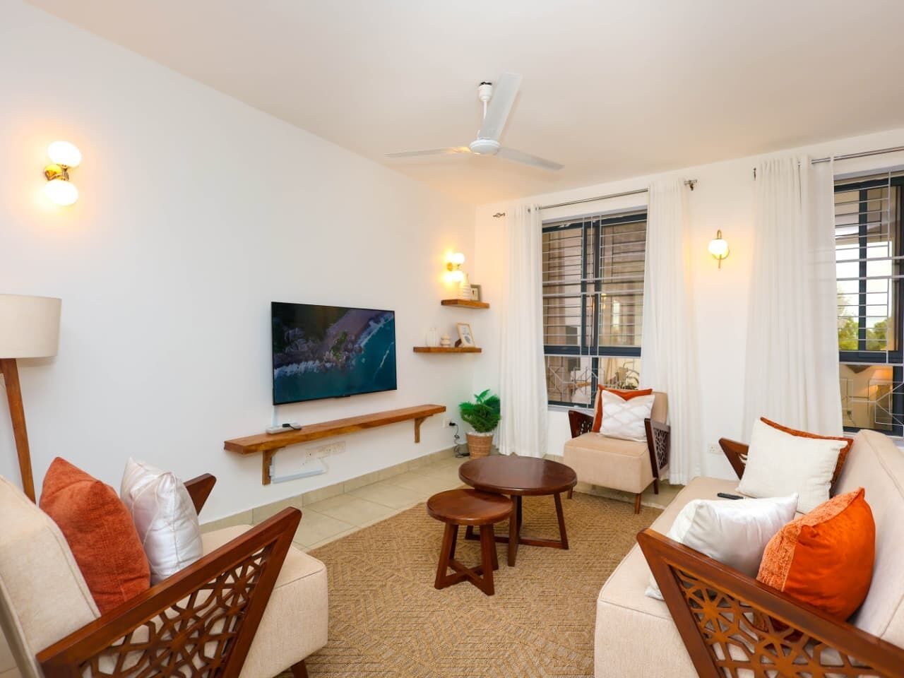 Sala de estar con televisor, asientos, ventilador de techo y ventana con cortinas.