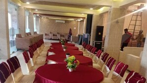 A banquet hall with round tables, white chairs, and red tablecloths. - MEERA MADHAV RESORT (Mathura)
