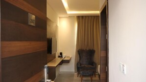 A hotel room with a wooden wall, a flat-screen TV, a chair, a small table, and a window with curtains. - MEERA MADHAV RESORT (Mathura)