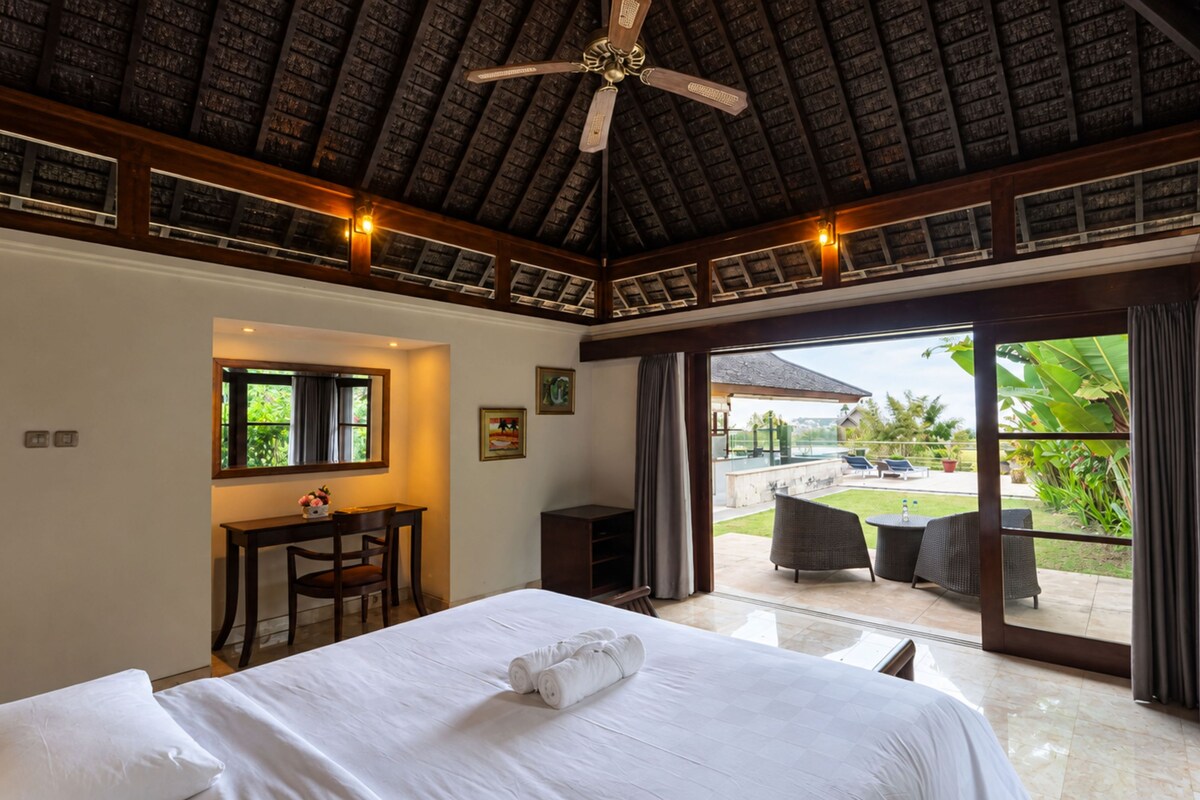 Ein Hotelzimmer mit Bett, Schreibtisch, Stuhl, Deckenventilator und Blick ins Freie.