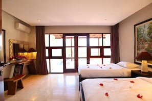 Ein Hotelzimmer mit zwei Betten, einem Schreibtisch mit Lampe, einem Spiegel und einem großen Fenster mit Vorhängen.