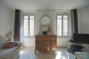 Ein Zimmer mit einer Couch, einem Schminktisch, einem Fernseher und einem Fenster mit Vorhängen.