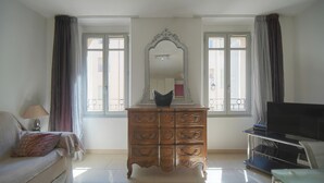 Una habitación con sofá, cómoda, televisor y ventana con cortinas.