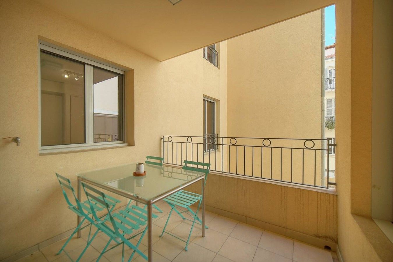 Ein Balkon mit Glastisch und Stühlen, ein Fenster und einem Metallgeländer.