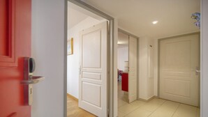 Un pasillo con puertas blancas, una puerta roja y suelo de baldosas.