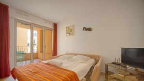 Een slaapkamer met een bed, een televisie, een glazen kast en een schuifpui naar een balkon.