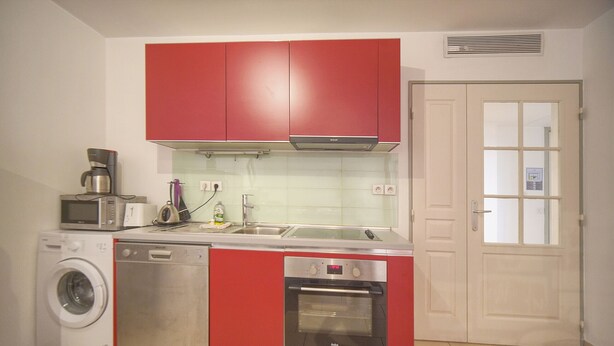 Een kleine keuken met een wasmachine, magnetron, oven en rode kastjes.