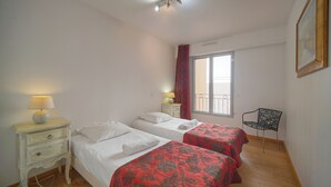 Een slaapkamer met twee bedden, een nachtkastje met een lamp, een stoel en een raam met gordijnen.