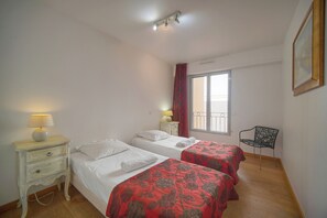 Ein Schlafzimmer mit zwei Betten, einem Nachttisch mit Lampe, einem Sessel und einem Fenster mit Vorhängen.
