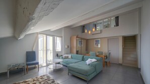 A living room with a sofa, a chair, a small table, and a staircase leading to an upper level. - FRGK - SUQUET DUPLEX WITH VIEWS OF THE HARBOR AND THE PALACE - 2BR (Cannes)