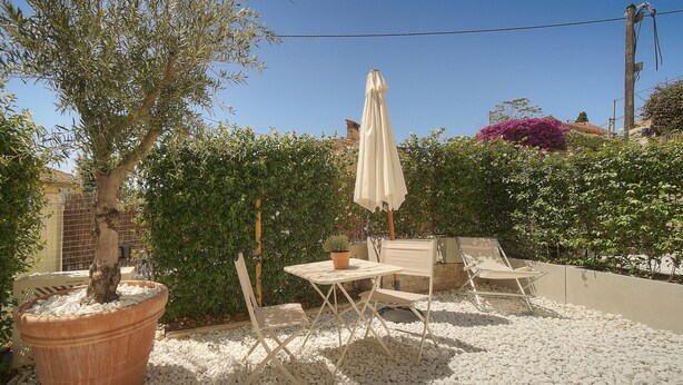 Een terras met een tafel en stoelen, omringd door witte kiezels, een plant in pot en een witte parasol.