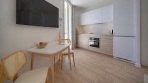 Een moderne keuken met witte kasten, een inbouwoven en een eethoek met een tafel en stoelen.