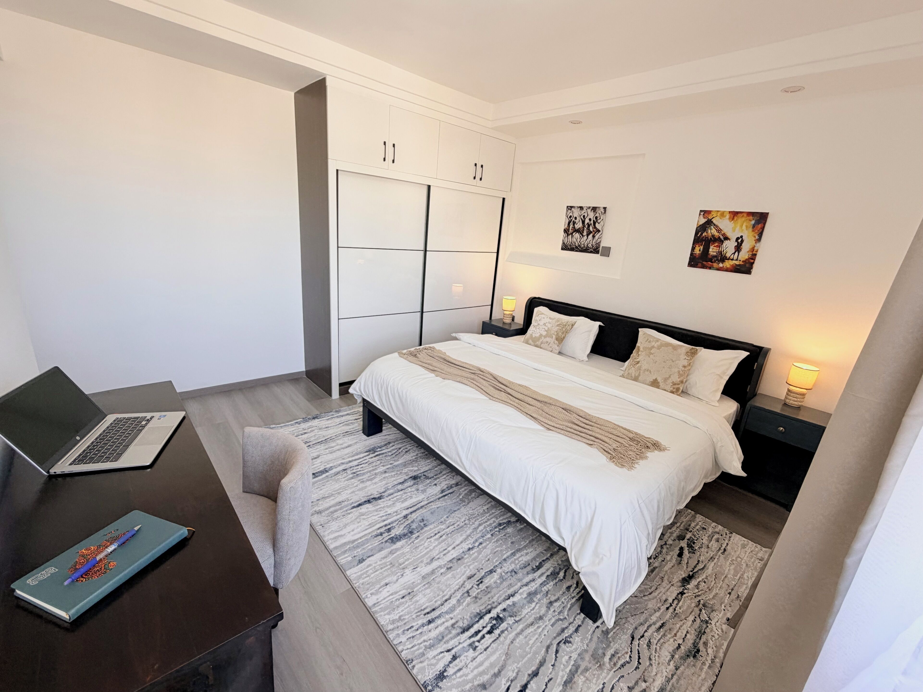 Une chambre à coucher moderne avec un lit, des tables de chevet, un bureau avec un ordinateur portable et une chaise.